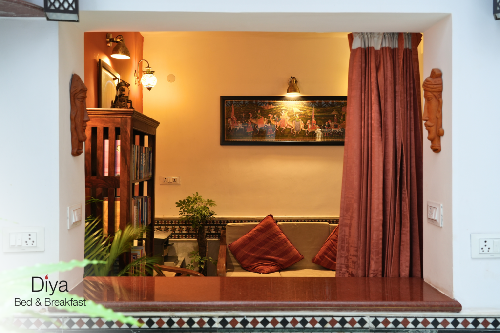 Cozy reading nook at Diya Bed & Breakfast with warm lighting, traditional artwork, a cushioned sofa, and a wooden bookshelf.