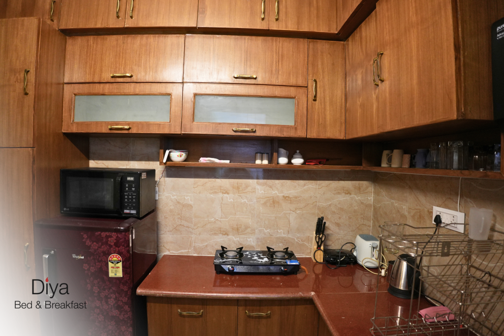 Close-up view of the kitchen at Diya Bed & Breakfast, featuring a microwave, gas stove, electric kettle, toaster, and neatly arranged kitchenware.