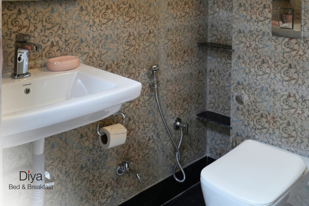 Modern bathroom at Diya Bed & Breakfast with a white sink, wall-mounted toilet, handheld bidet, toilet paper holder, and patterned wall tiles.