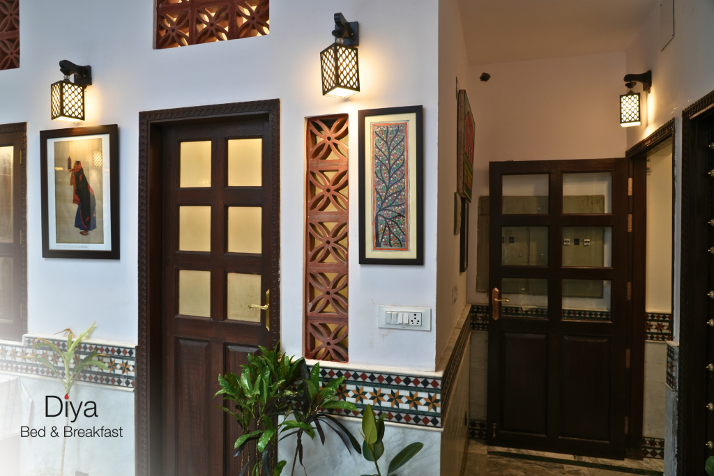 Well-lit hallway at Diya Bed & Breakfast with wooden doors, decorative wall tiles, framed artwork, and indoor plants.