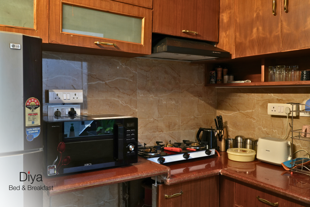 Close-up view of the kitchen at Diya Bed & Breakfast, featuring a microwave, gas stove, electric kettle, toaster, and neatly arranged kitchenware.