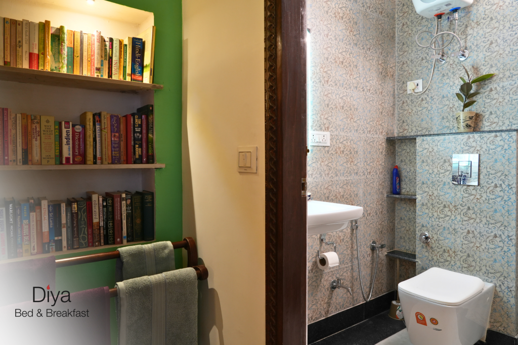 Bookshelf and towel rack next to a bathroom at Diya Bed & Breakfast, featuring a neatly arranged toilet, sink, and water heater.