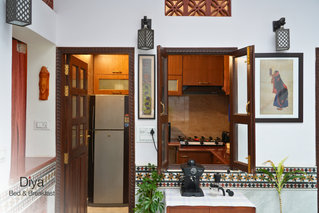 Interior view of the kitchen at Diya Bed & Breakfast, featuring wooden cabinetry, a stainless steel refrigerator, a coffee machine, and decorative wall art.