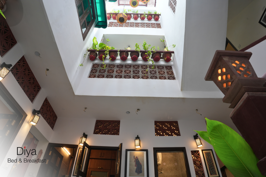 View of the open atrium at Diya Bed & Breakfast, looking upward to balconies adorned with red potted plants and traditional latticework.