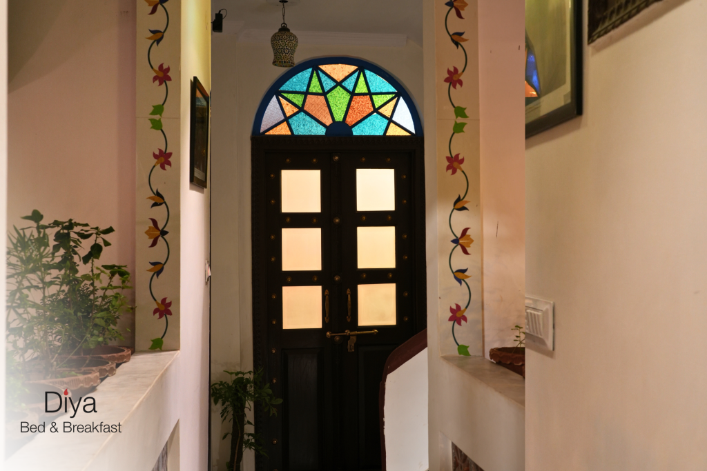 Entrance hallway with a dark wooden door featuring frosted glass panels and a colorful stained-glass arched window above, framed by floral wall paintings.