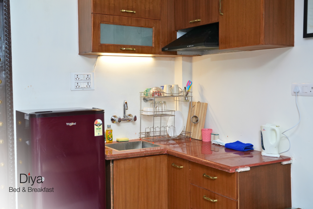 Compact kitchen area at Diya Bed & Breakfast with a mini fridge, sink, countertop, kettle, and wooden cabinets.