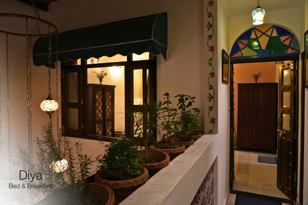 Night view of a warmly lit corridor at Diya Bed & Breakfast with potted plants, colourful stained glass, and decorative hanging lamps.