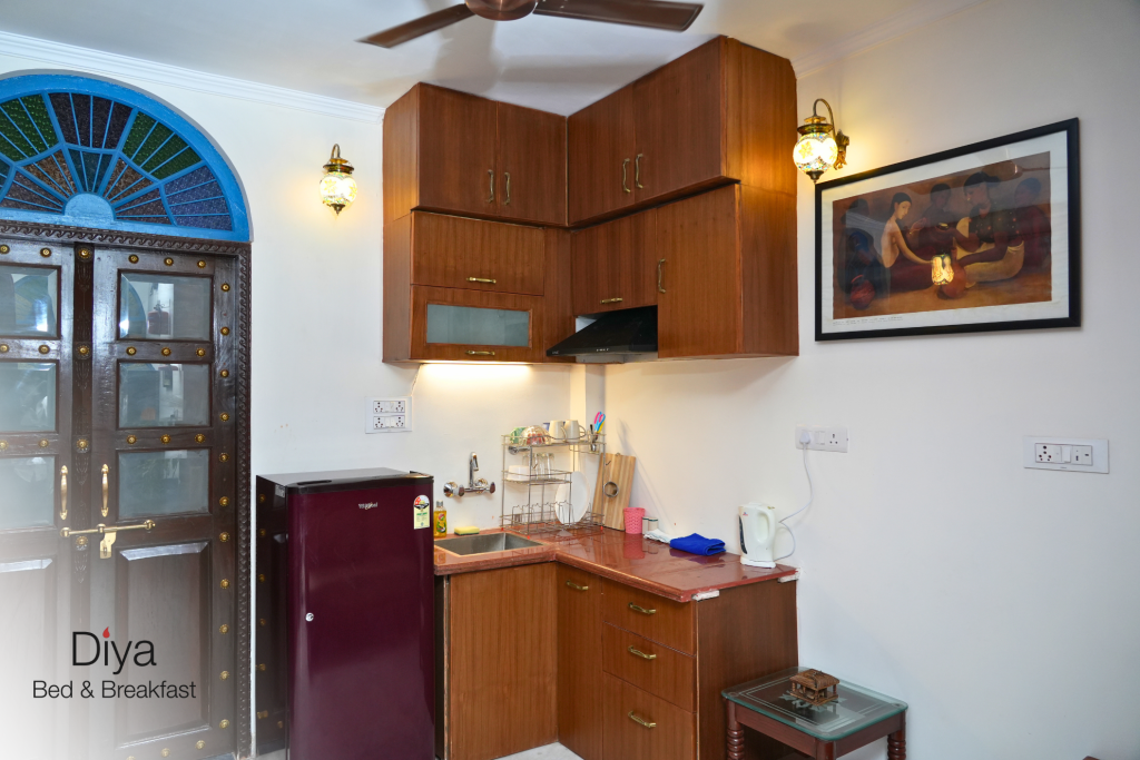 Compact kitchen area at Diya Bed & Breakfast with a mini fridge, sink, countertop, kettle, and wooden cabinets.