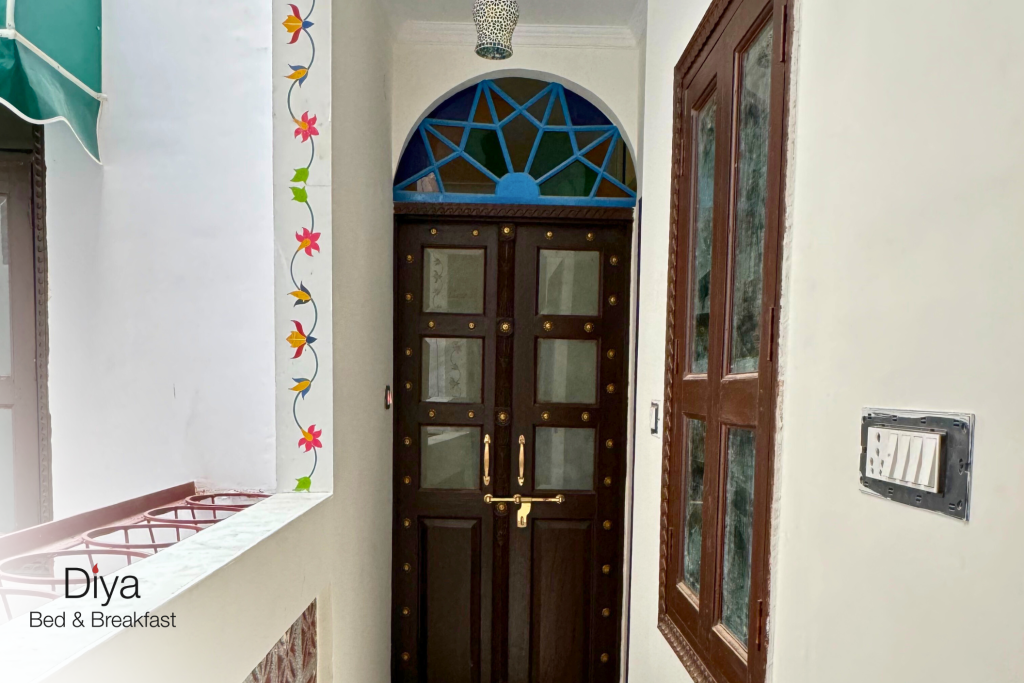 Entrance hallway with a dark wooden door featuring frosted glass panels and a colorful stained-glass arched window above, framed by floral wall paintings.