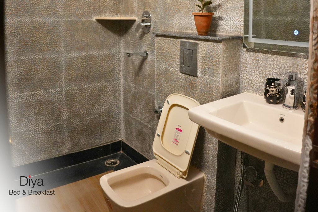 Modern bathroom at Diya Bed & Breakfast with a white sink, wall-mounted toilet, handheld bidet, toilet paper holder, and patterned wall tiles.