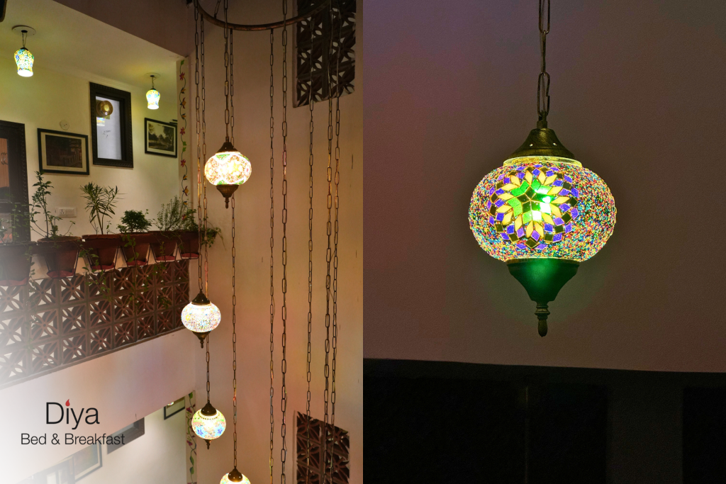 Colorful mosaic glass pendant lamps hanging in a vertical arrangement at Diya Bed & Breakfast, with a close-up of one lamp showcasing intricate green, blue, and yellow patterns.