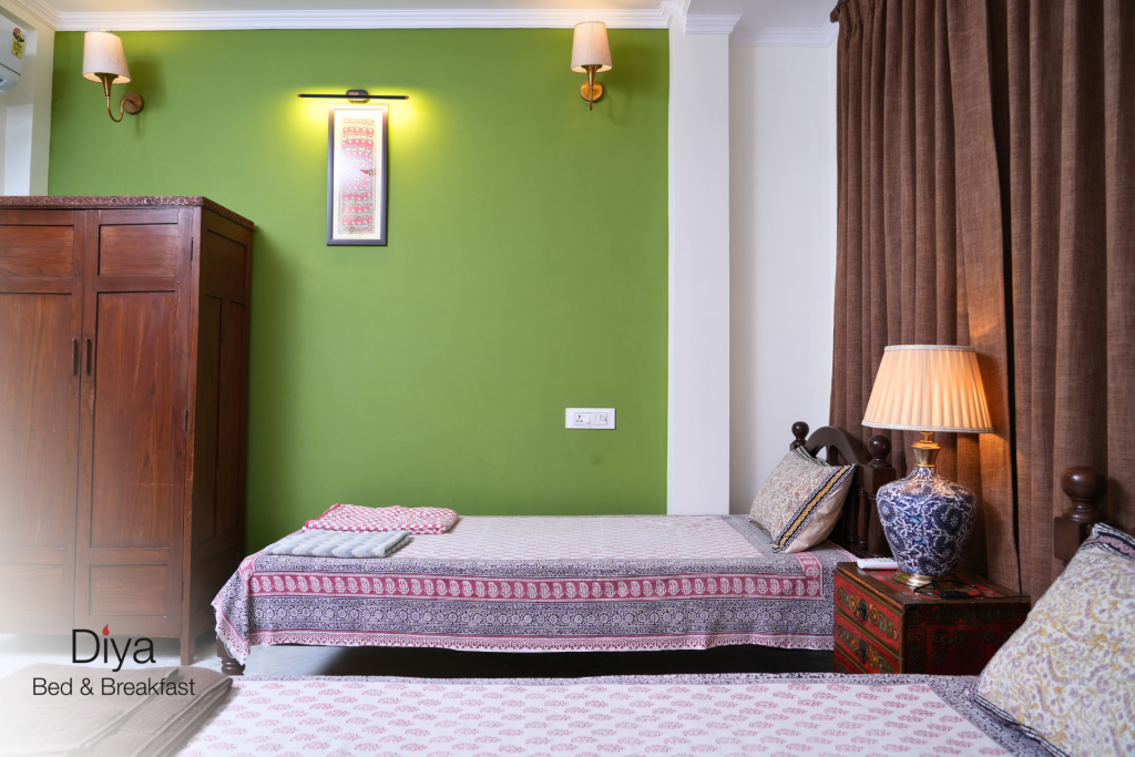 Bright and cozy twin bedroom with green accent wall, patterned bedspreads, and warm lighting at Diya Bed & Breakfast.