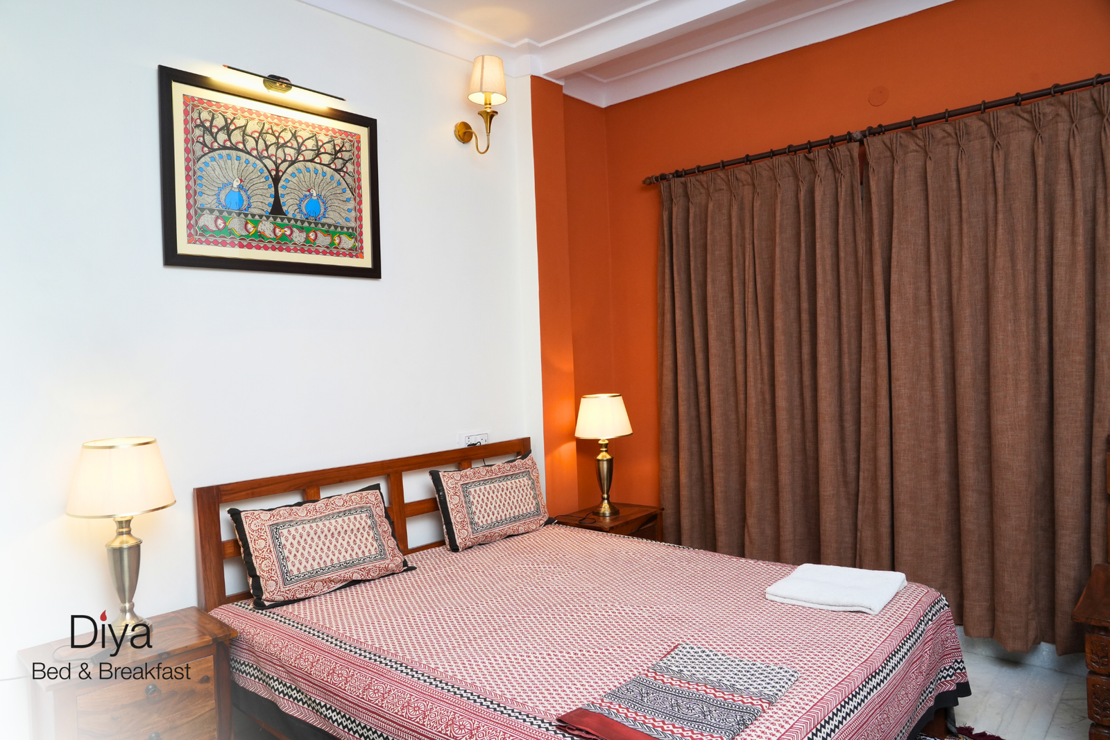 Warm bedroom with wooden furniture, orange accent wall, and traditional framed artwork above the bed.