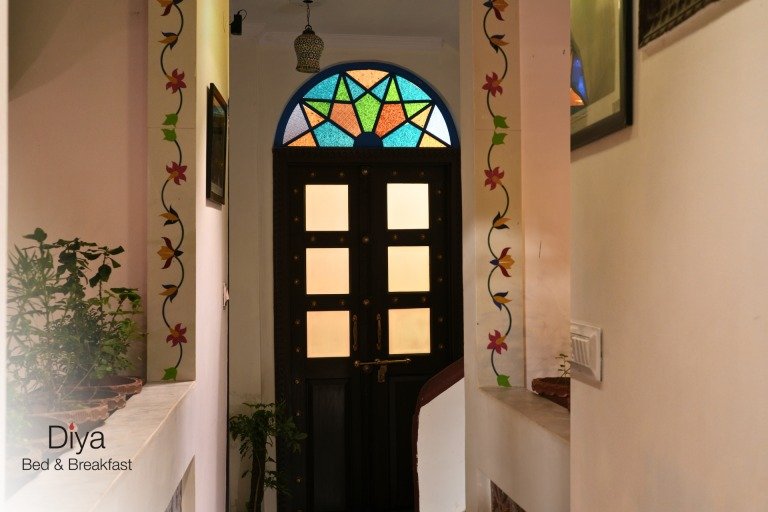 Entrance hallway with a dark wooden door featuring frosted glass panels and a colourful stained-glass arched window above, framed by floral wall paintings.
