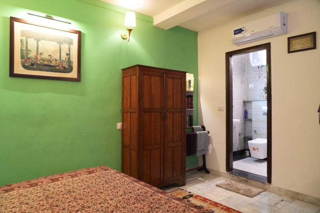 Bedroom with green accent wall, wooden wardrobe, framed artwork, and an attached bathroom with tiled walls.