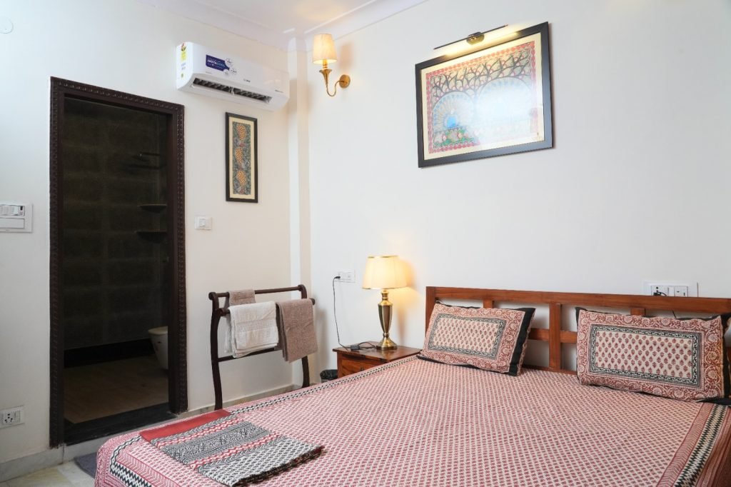 Cozy bedroom with a double bed, patterned bedding, bedside lamp, wall art, and an attached bathroom.