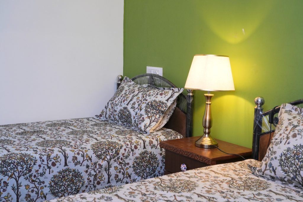 Two single beds with floral-patterned bedding and a bedside lamp against a green accent wall.