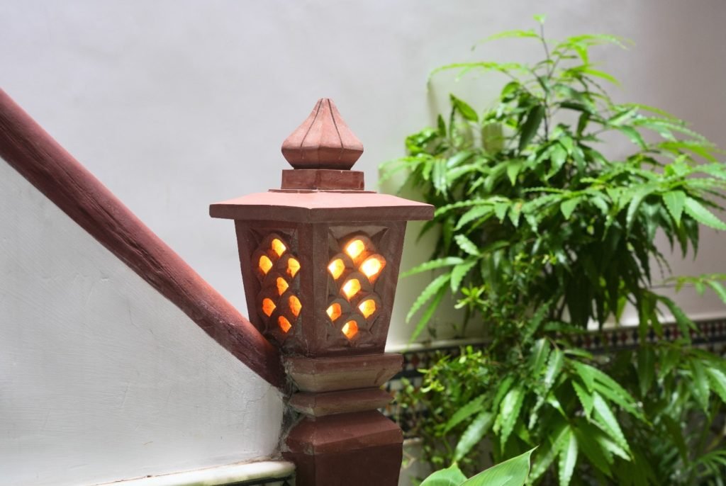 Close-up of a decorative terracotta lantern on a staircase with warm lighting and green plants in the background.