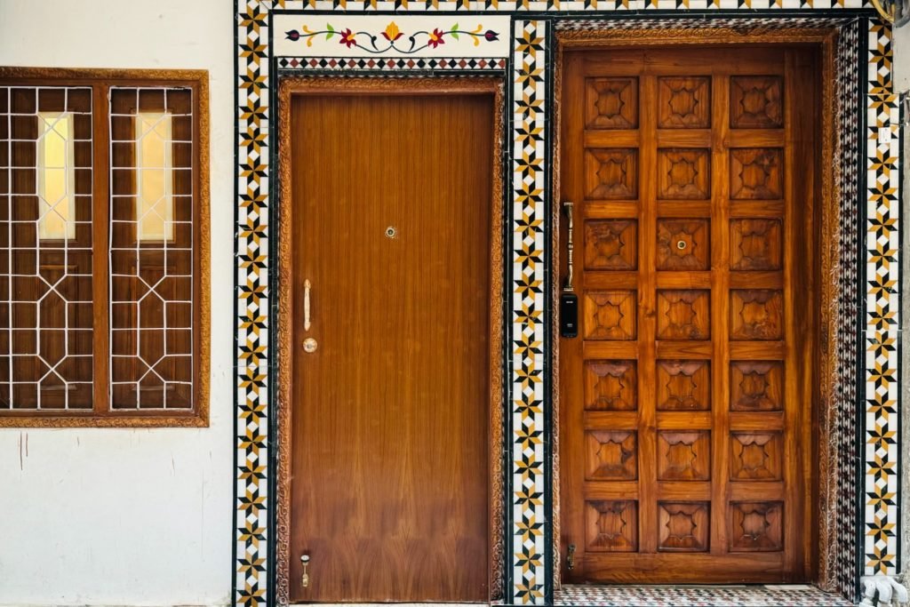 Two wooden doors with decorative tile borders, one plain and one carved, next to a wooden-framed window with a geometric grille.